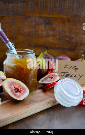 Fresh ripe Autumn fruit, figs, with fig jelly preserve in jar on cutting board against dark wood background. Stock Photo