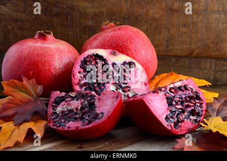 Stack of fresh pomegranates with cut slices on Autumn Fall leaves against a dark wood vintage background. Stock Photo