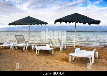 Two parasol and plastic chairs on the sand beach Stock Photo