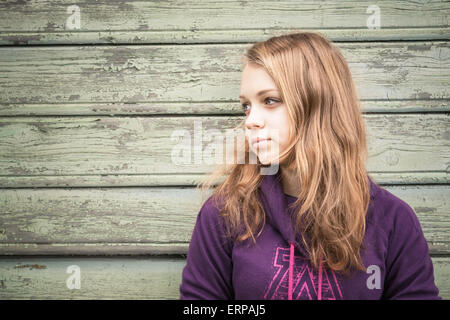 Beautiful blond Caucasian teenage girl, closeup profile outdoor portrait over green wooden wall Stock Photo