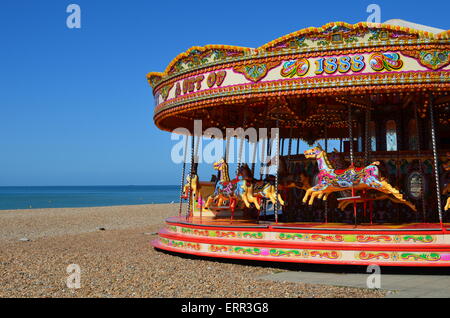 Traditional Victorian fairground  carousel on Brighton pebble beach during the summer. Stock Photo
