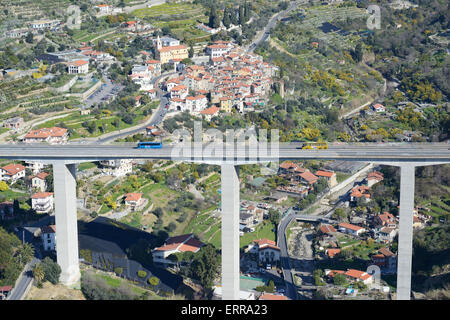 AERIAL VIEW. Village behind a highway bridge on a hillside with mimosa in full bloom. Borghetto San Nicolò, Province of Imperia, Liguria, Italy. Stock Photo