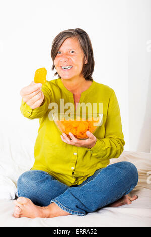woman sitting in bed with potato chips and offering one chip Stock Photo