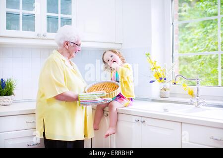 Happy beautiful great grandmother and her adorable granddaughter, curly toddler girl in colorful dress, baking an apple pie Stock Photo