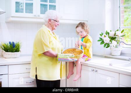 Happy beautiful great grandmother and her adorable granddaughter, curly toddler girl in colorful dress, baking an apple pie Stock Photo