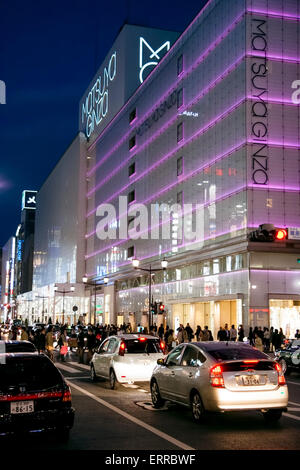 Tokyo Ginza at night. View along and across street with traffic of the Matsuya Ginza department store building illuminated in pink strip lighting. Stock Photo