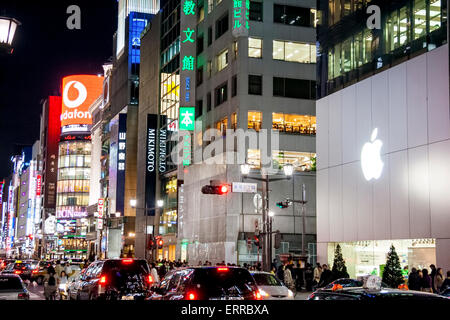 The Ginza at night. View along traffic filled street with the Apple Store in foreground and in background the Sanai building on the Ginza crossing. Stock Photo