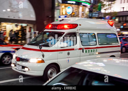 Japan, the Ginza in Tokyo. White ambulance speeding past with red flashing lights, panning focus on ambulance with motion blur on surrounding street. Stock Photo