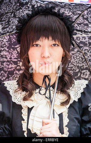 Harajuku, Tokyo. Face, Japanese young woman dressed in Goth Lolita style in black Victorian maid costume and holding black lacy umbrella. Eye-contact. Stock Photo