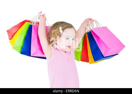 Adorable little girl with curly hair wearing pink dress is happy after sale and special offer shopping showing her colorful bags Stock Photo
