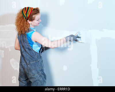 Portrait of a smiling young woman construction worker patching up drywall with mud Stock Photo