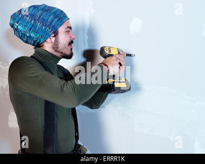 Portrait of a smiling young man contractor worker mounting drywall with a screw gun renovating interior Stock Photo