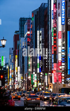 The fashion Ginza in Tokyo at night. View along and across traffic filled street with row of tall buildings and illuminated vertical signs. Stock Photo