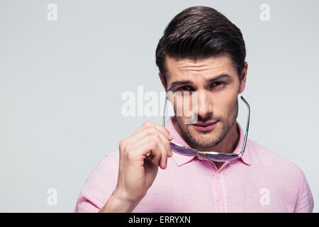 Young stylish man holding glasses and looking at camera over gray background Stock Photo