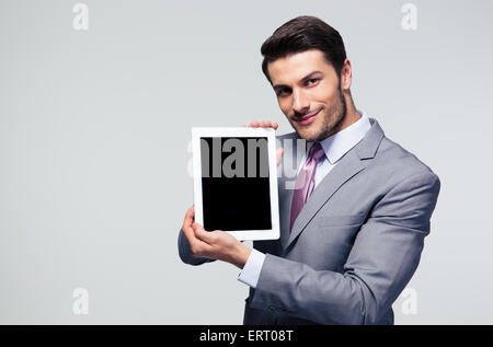 Happy businessman showing blank tablet computer screen over gray background. Looking at camera Stock Photo
