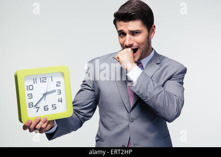 Worried businessman holding clock and looking at camera over gray background Stock Photo