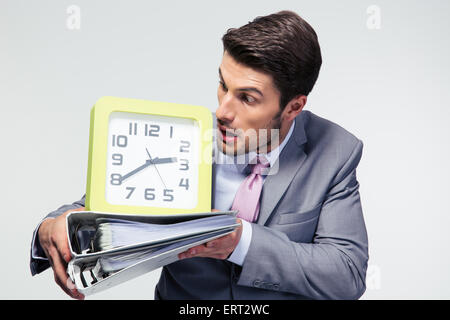 Businessman holding folders and looking on clock over gray background Stock Photo