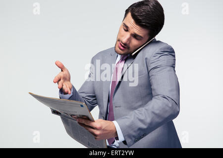 Businessman talking on the phone and reading newspaper over gray background Stock Photo