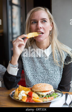 blond woman siting in restaurant with a burger Stock Photo