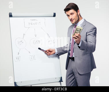 Businessman making presentation on flipchart and holding US dollar bills ovver gray background. Looking at camera Stock Photo