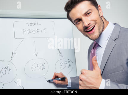 Happy businessman writing on a flipchart and showing thumb up. Looking at camera Stock Photo