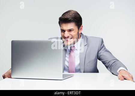 Worried businessman sitting at the table with laptop over gray background Stock Photo