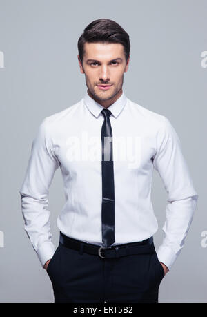 Young businessman standing with hands in pocket over gray background Stock Photo