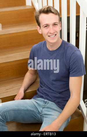 blond young man sitting on stairs and smiles Stock Photo