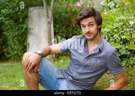 young casual man posing seated, smiling at the camera, outdoors Stock Photo