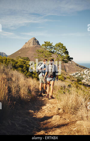Portrait of couple of hikers walking through pathway on mountain. Man and woman enjoying summer vacation in countryside during a Stock Photo