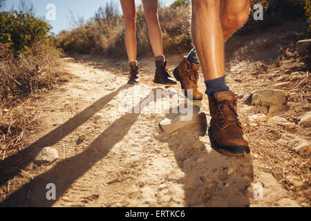 Close-up of legs of young hikers walking on the country path. Young couple trail waking. Focus on hiking shoes. Stock Photo