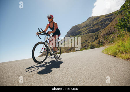 Woman competing in the cycling leg of a triathlon with competitor. Triathletes riding bicycle on open road. Stock Photo
