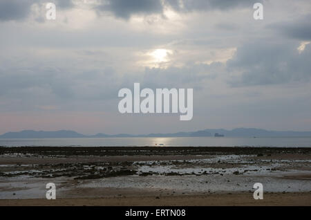 Sun setting behind clouds over Nong Thale Beach at low tide in Krabi Province, Thailand Stock Photo