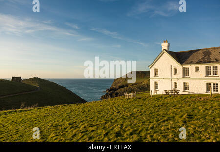 Doyden Castle on headland and house overlook the sea at sunset at Port Quin, Cornwall, England, UK Stock Photo