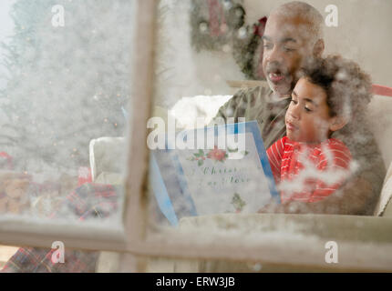 Mixed race grandfather reading to grandson behind window at Christmas Stock Photo