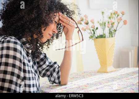 Anxious mixed race woman sitting at table Stock Photo