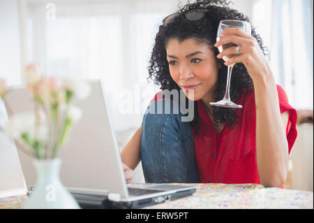 Mixed race woman drinking wine and using laptop Stock Photo