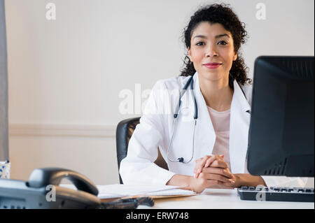 Mixed race doctor sitting at desk in office Stock Photo
