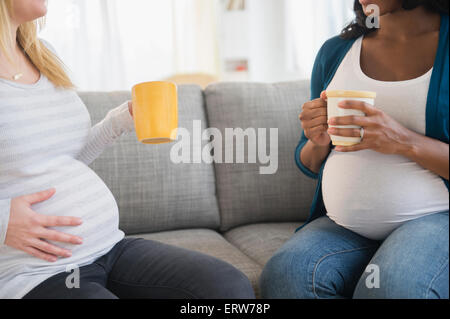 Pregnant women drinking coffee and talking on sofa Stock Photo