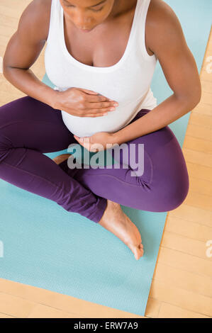 Black pregnant woman sitting on exercise mat holding stomach Stock Photo