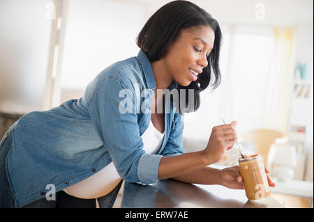 Black pregnant woman eating peanut butter in kitchen Stock Photo