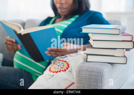 Black pregnant woman reading books on sofa Stock Photo