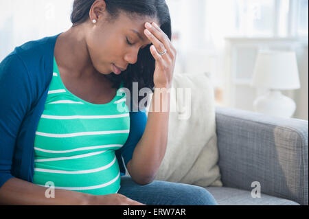 Anxious Black pregnant woman rubbing forehead on sofa Stock Photo