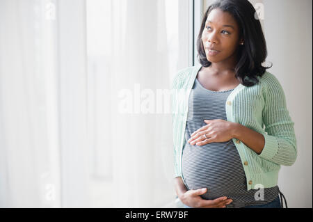 Black pregnant woman holding her stomach at window Stock Photo