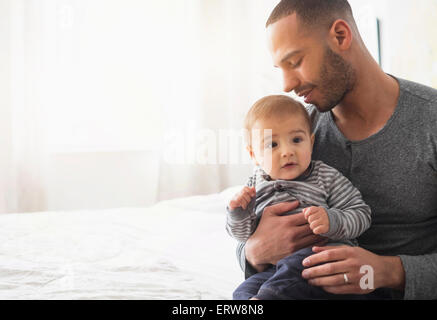 Smiling father holding baby son on bed Stock Photo