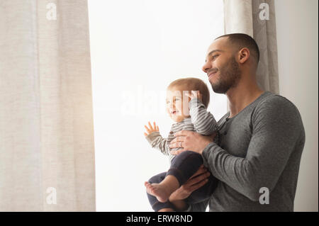 Smiling father and baby son looking out window Stock Photo