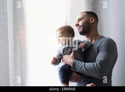 Smiling father and baby son looking out window Stock Photo