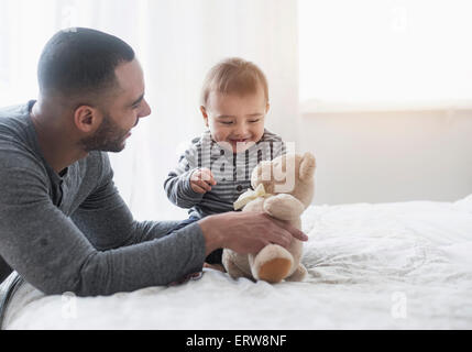Smiling father playing with baby son on bed Stock Photo