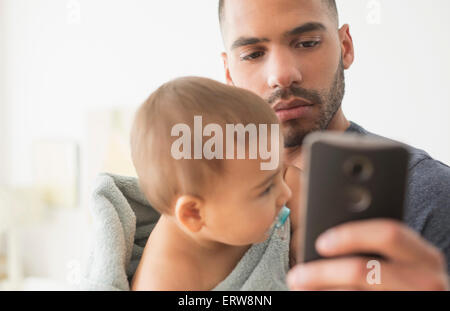 Father holding baby son and using cell phone Stock Photo