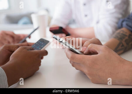 Close up of friends texting with cell phones at table Stock Photo